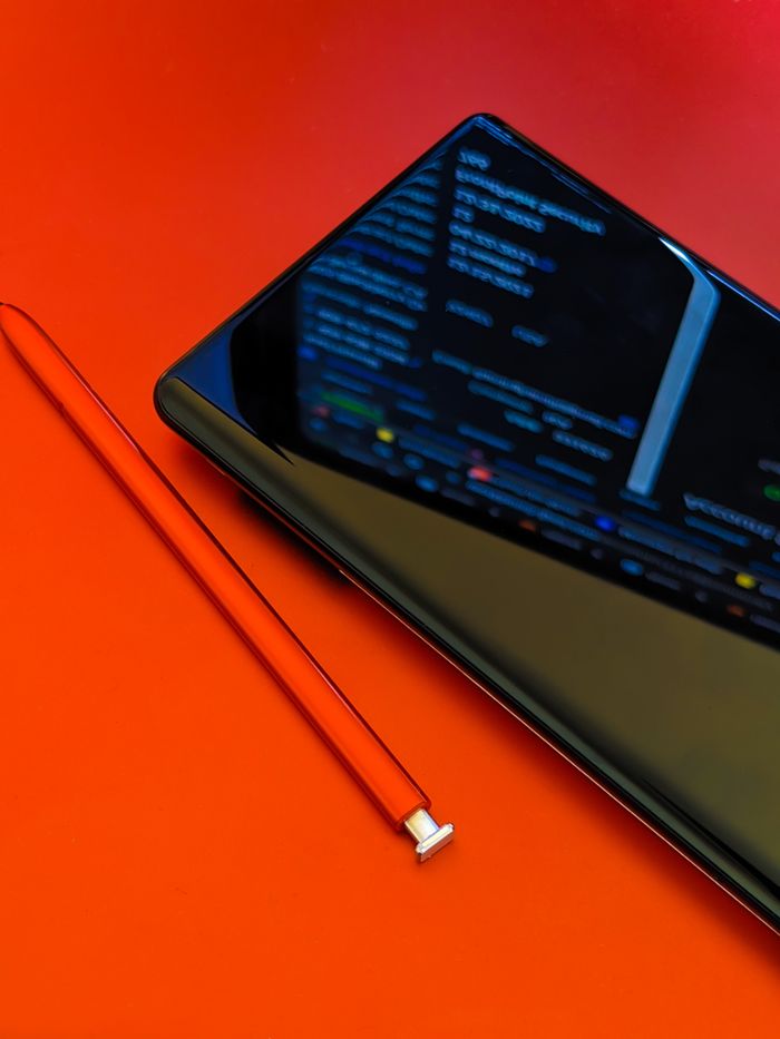 Vue rapprochée d’un smartphone accompagné d’un stylet sur une surface rouge éclatante, mettant en avant la technologie moderne.